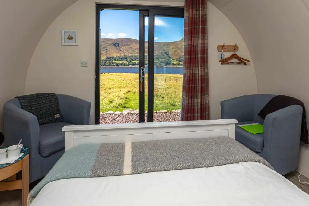 a bedroom with a bed and two chairs and a window at Loch Broom Glamping in Garve