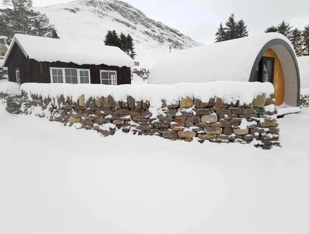 a stone wall covered in snow in front of a building at Loch Broom Glamping in Garve