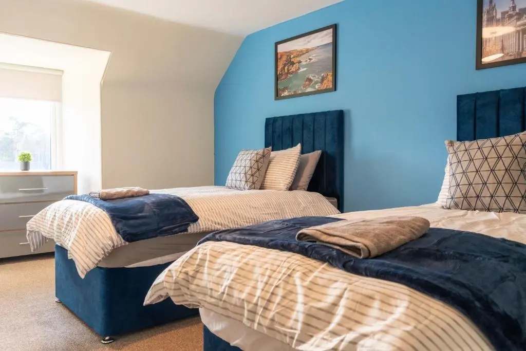 two beds in a room with blue walls at Rosewood Cottage in Cornhill