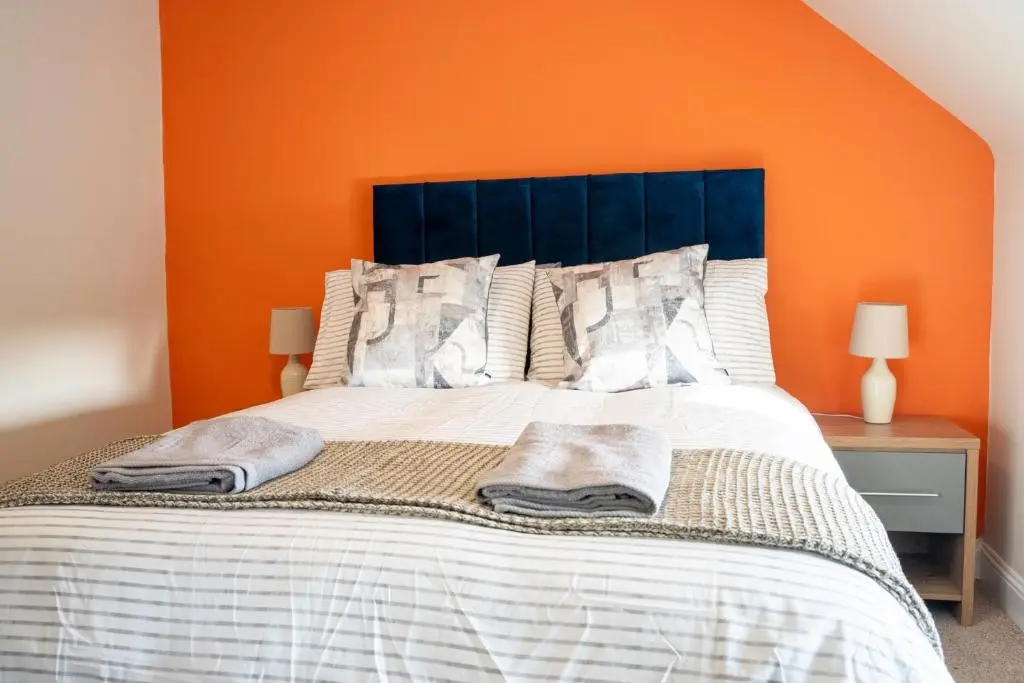 a bed with a blue headboard and an orange wall at Rosewood Cottage in Cornhill