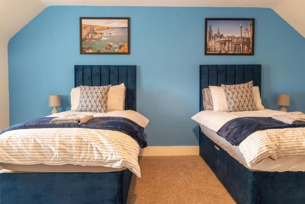 two beds in a room with blue walls at Rosewood Cottage in Cornhill