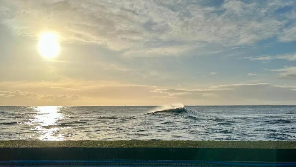 a wave in the ocean with the sun in the sky at The Old Coastguard Station in Helmsdale