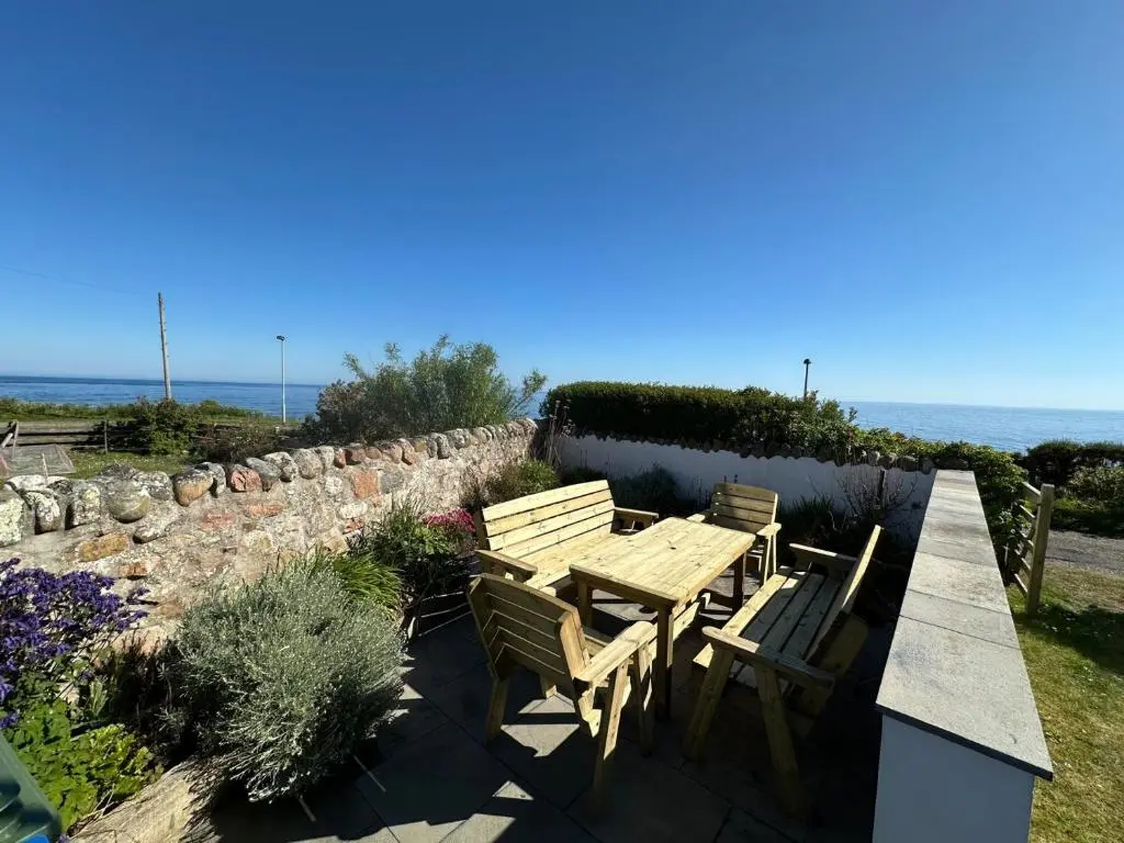 a wooden table and two chairs sitting next to a stone wall at The Old Coastguard Station in Helmsdale