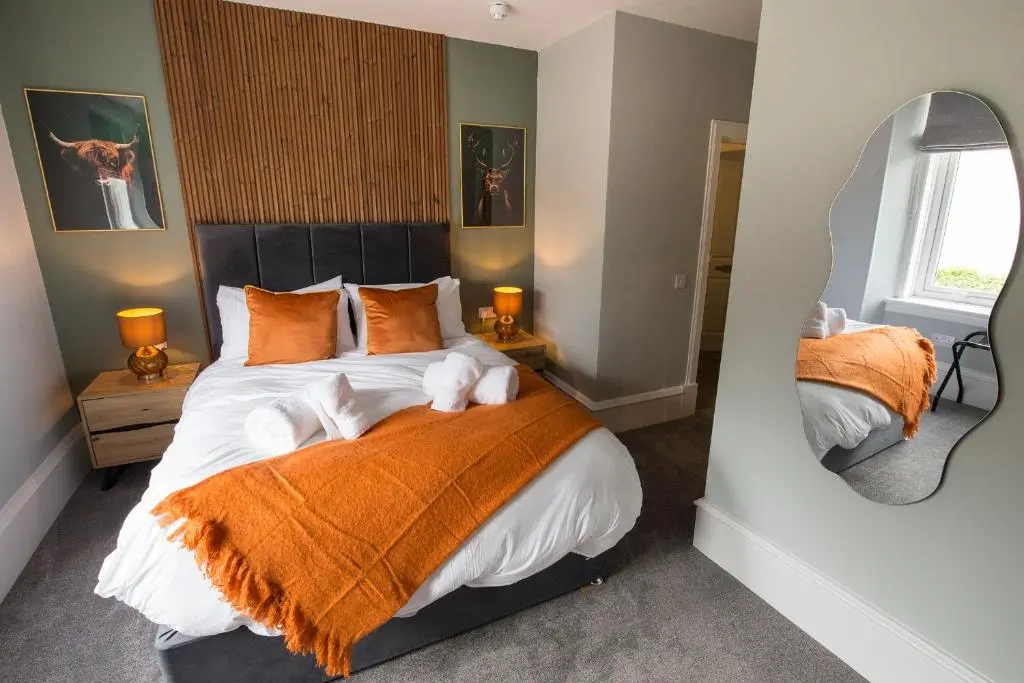 a bedroom with a bed with an orange blanket and a mirror at The Braeriach in Newtonmore