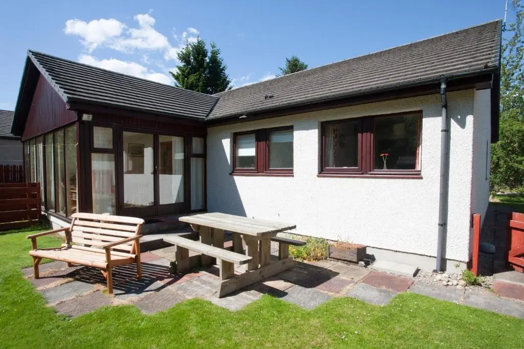 a picnic table and bench in front of a house at Heath Cottage, Tranquil Cottage by the Woods in Boat of Garten