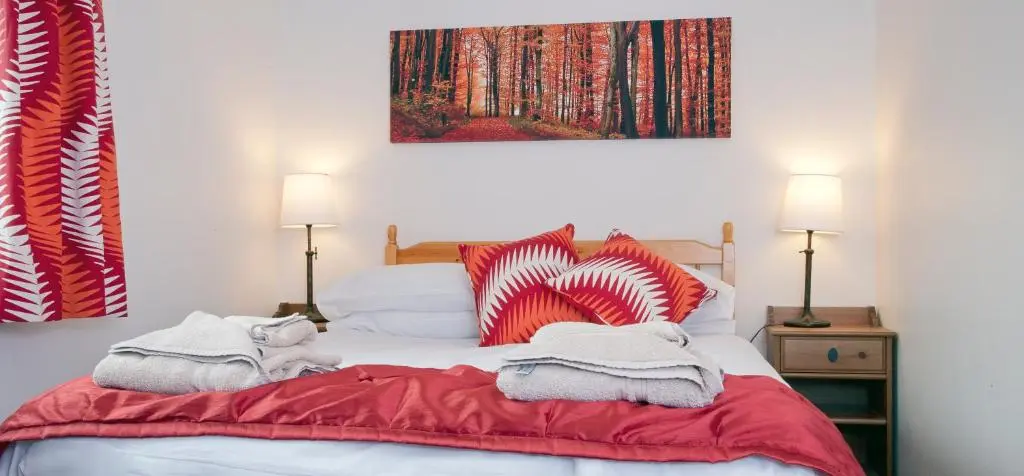 a bed with red and white blankets and pillows on it at Heath Cottage, Tranquil Cottage by the Woods in Boat of Garten