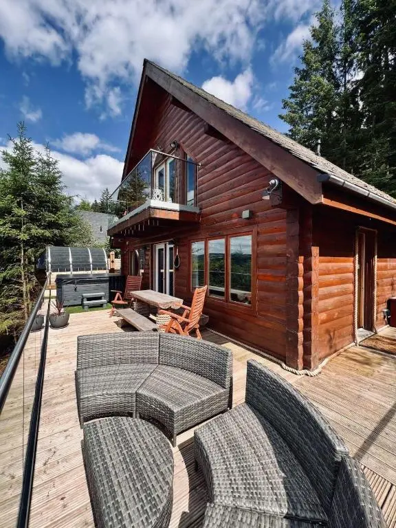 a log cabin with a deck with couches and a grill at Lodges On Loch Ness in Inverness