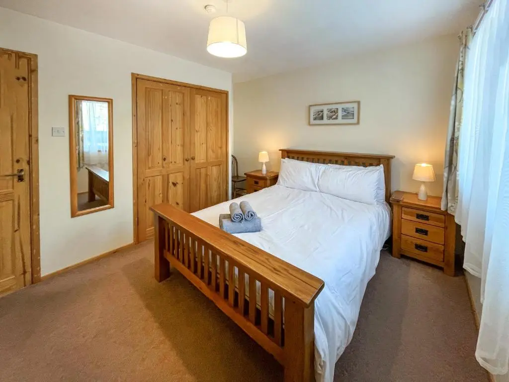 a bedroom with a large bed and a wooden bench at Lorien Cottage in Nethy Bridge