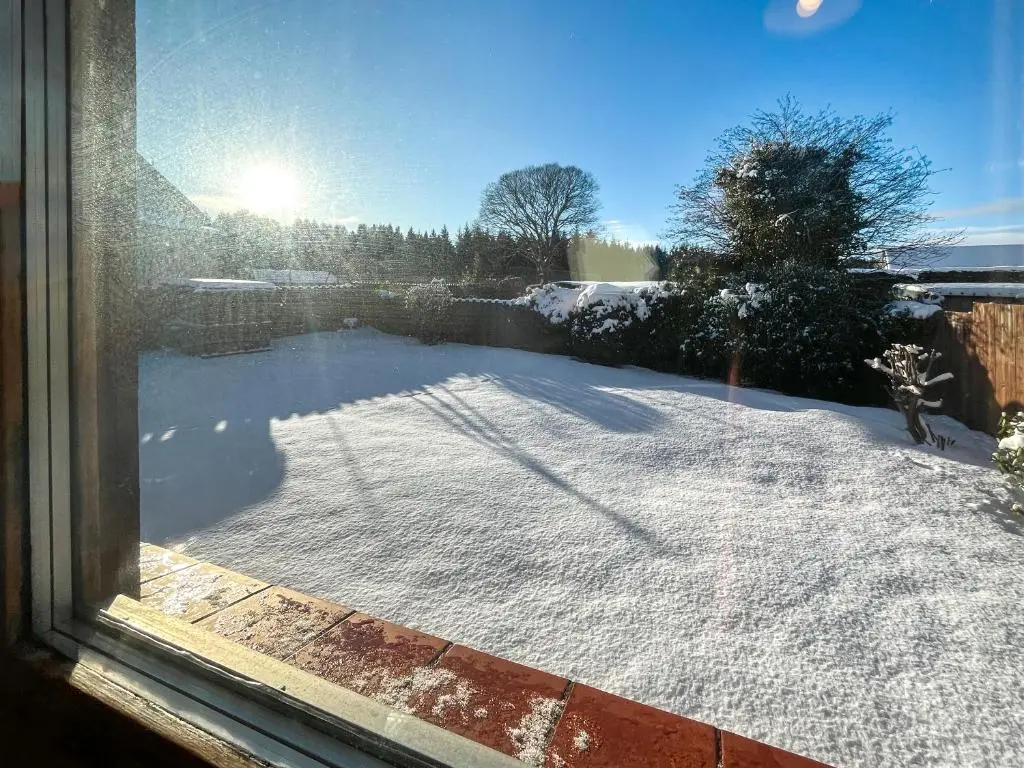 a view of a snow covered yard from a window at Lorien Cottage in Nethy Bridge