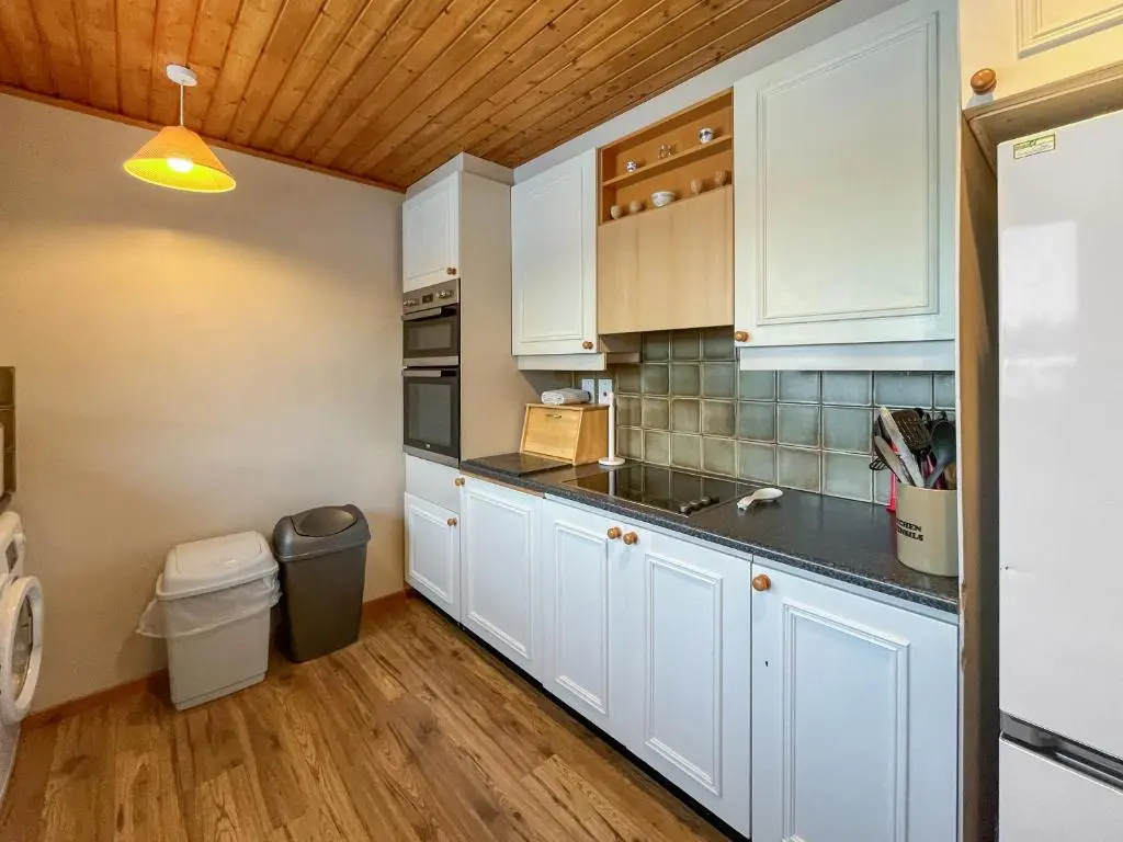 a kitchen with white cabinets and a trash can at Lorien Cottage in Nethy Bridge