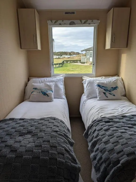 two beds in a small room with a window at Aurora on the Dunes- Cozy Coastal Retreat with Scenic Views in Lossiemouth