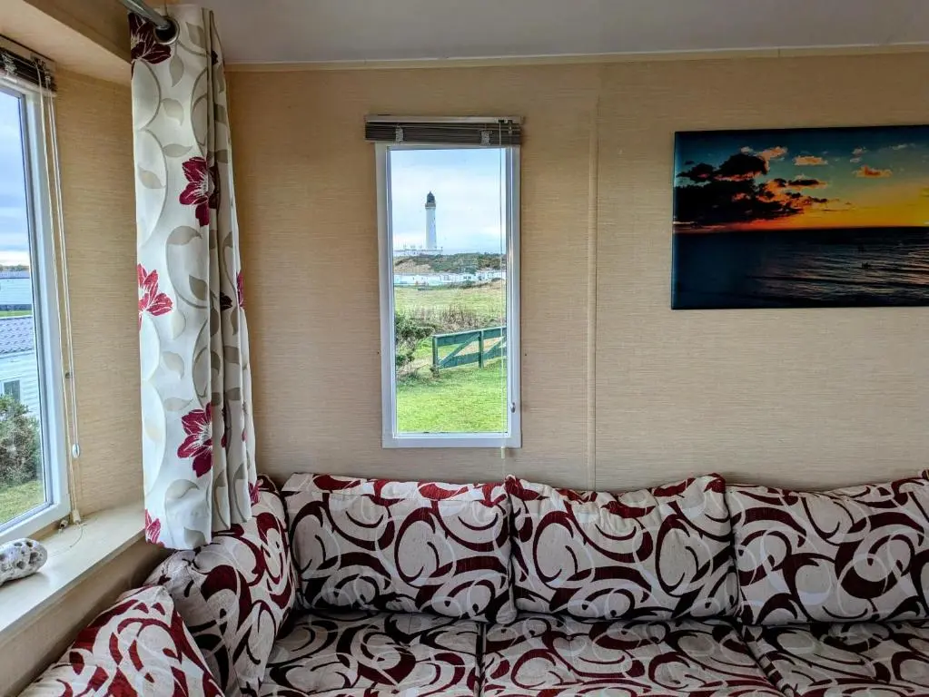 a couch sitting in a room with two windows at Aurora on the Dunes- Cozy Coastal Retreat with Scenic Views in Lossiemouth