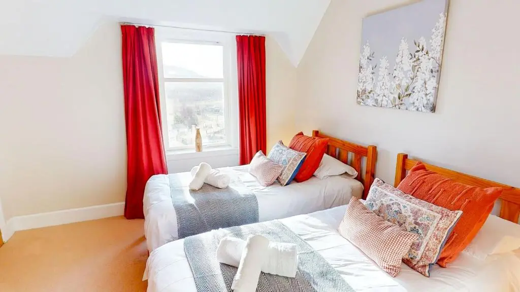 two beds in a room with red curtains and a window at Schoolhouse in Laggan