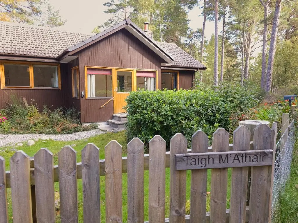 a wooden fence in front of a small house at Taigh Mathair Taigh Mathair in Nethy Bridge