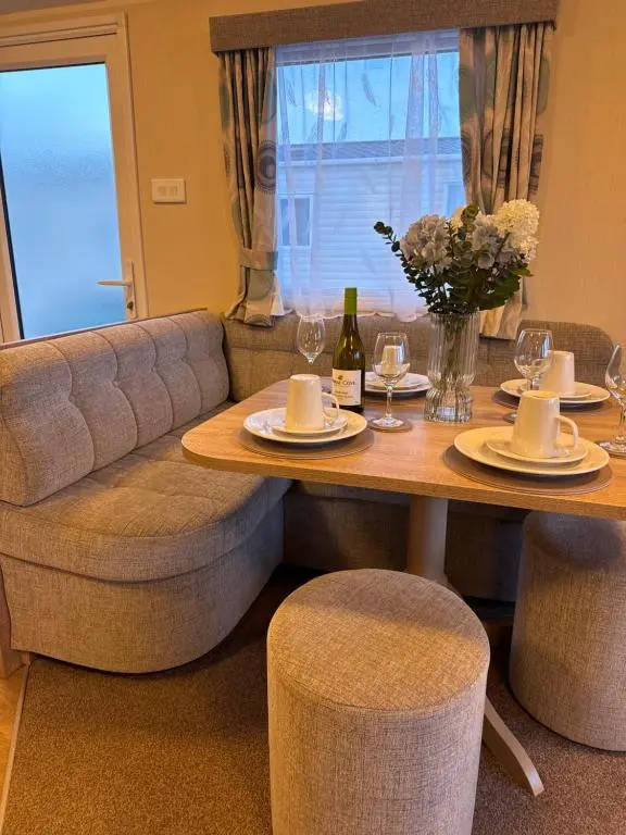 a dining room table with a couch and wine glasses at Little Cha-Am Caravan Hire at Silver Sands in Lossiemouth