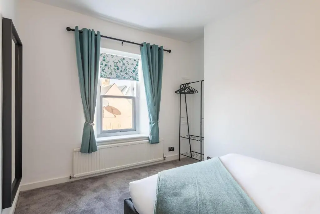 a bedroom with a bed and a window with blue curtains at Ness Heights, Spacious City Centre Townhouse in Inverness