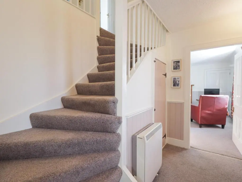 a staircase in a house with a red chair at Fuchsia Cottage in Fortrose