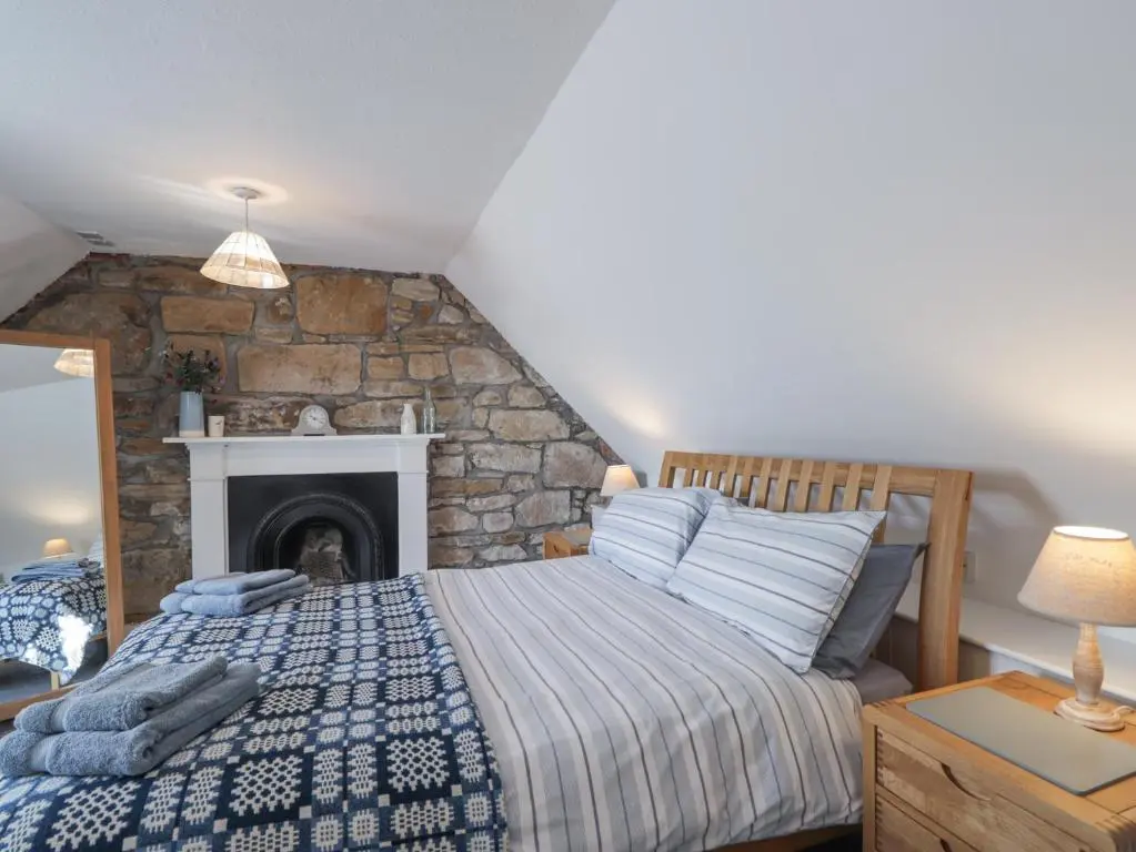 a bedroom with a bed with a stone fireplace at Fuchsia Cottage in Fortrose