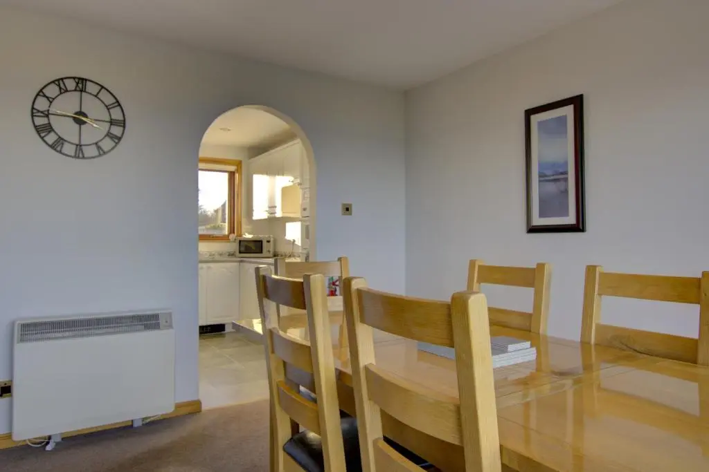 a dining room with a table and chairs and a clock at 2 Links View, Brora in Brora