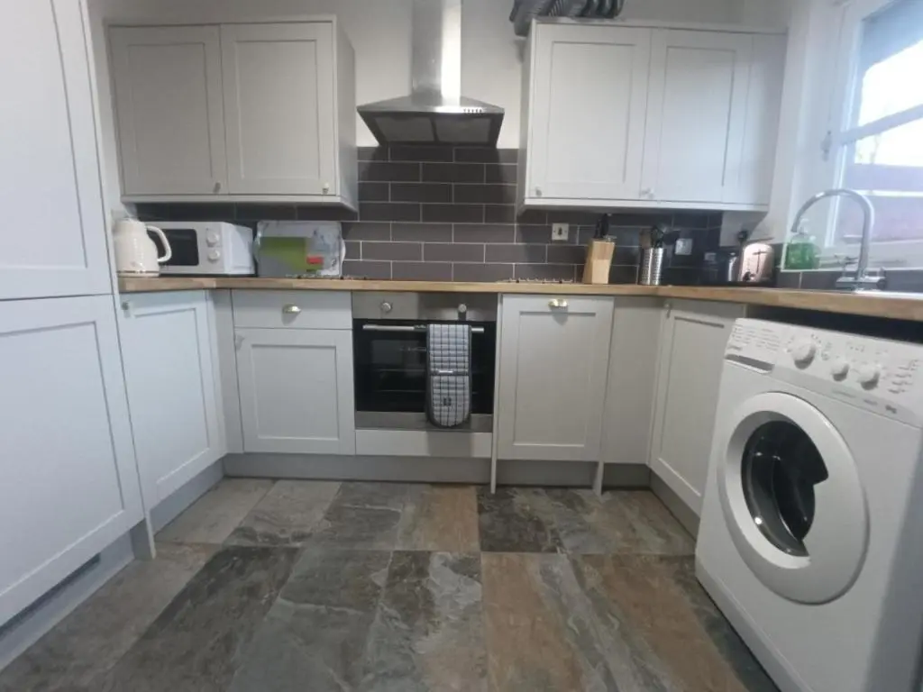 a kitchen with white cabinets and a washer at Steam Train Cottage in Aviemore