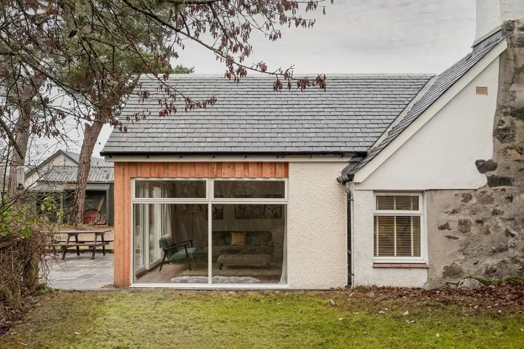 a white house with a large sliding glass door at The Old Smithy - Seasgair Lodges in Nethy Bridge