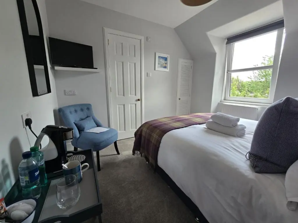 a bedroom with a bed and a chair and a window at Tullochard Guest House in Alness
