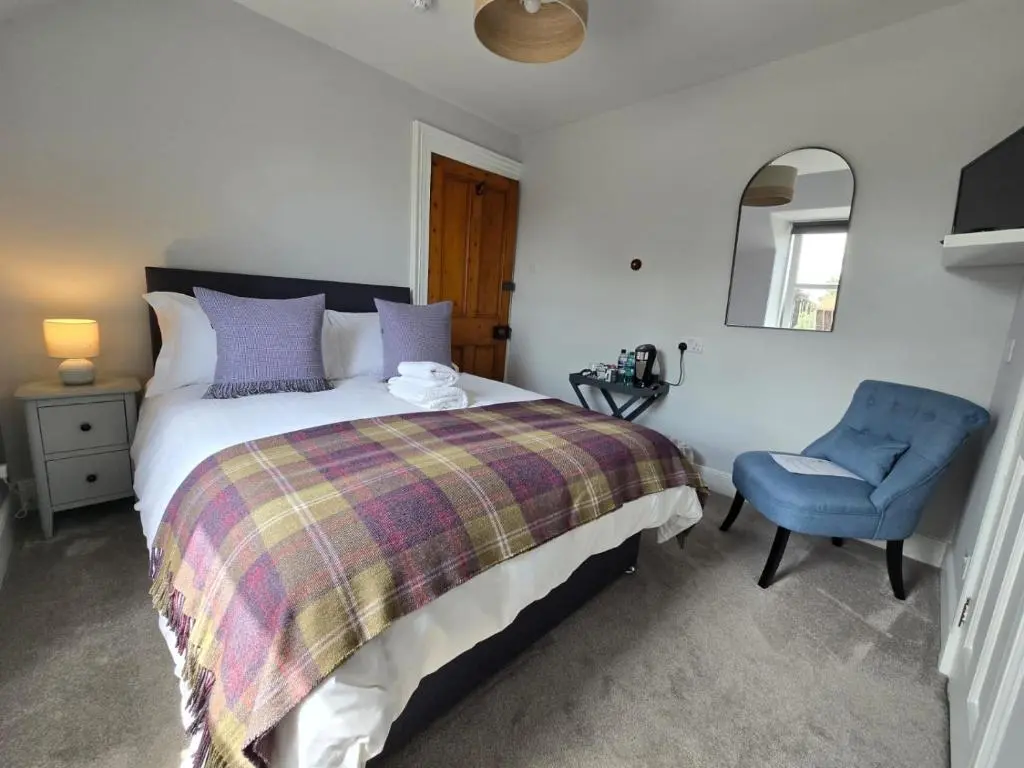 a bedroom with a bed and a blue chair at Tullochard Guest House in Alness