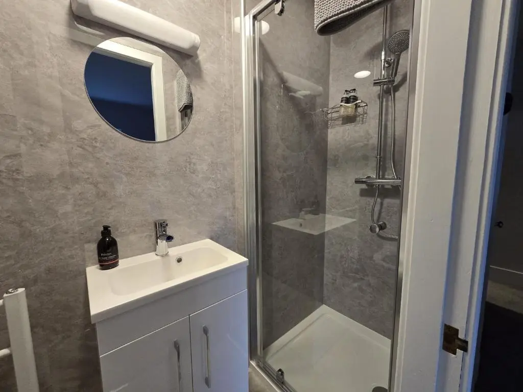a bathroom with a sink and a shower with a mirror at Tullochard Guest House in Alness