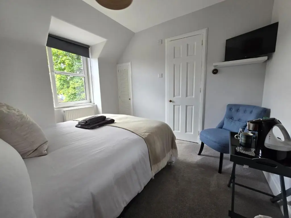 a bedroom with a bed and a blue chair at Tullochard Guest House in Alness