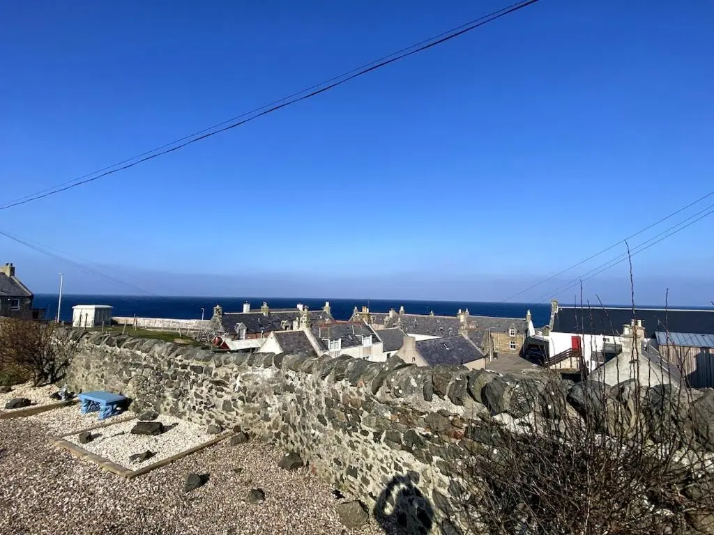 a stone wall with houses and the ocean in the background at Number Forty Two, Portsoy - A 3 bedroom cottage with sea views in Portsoy
