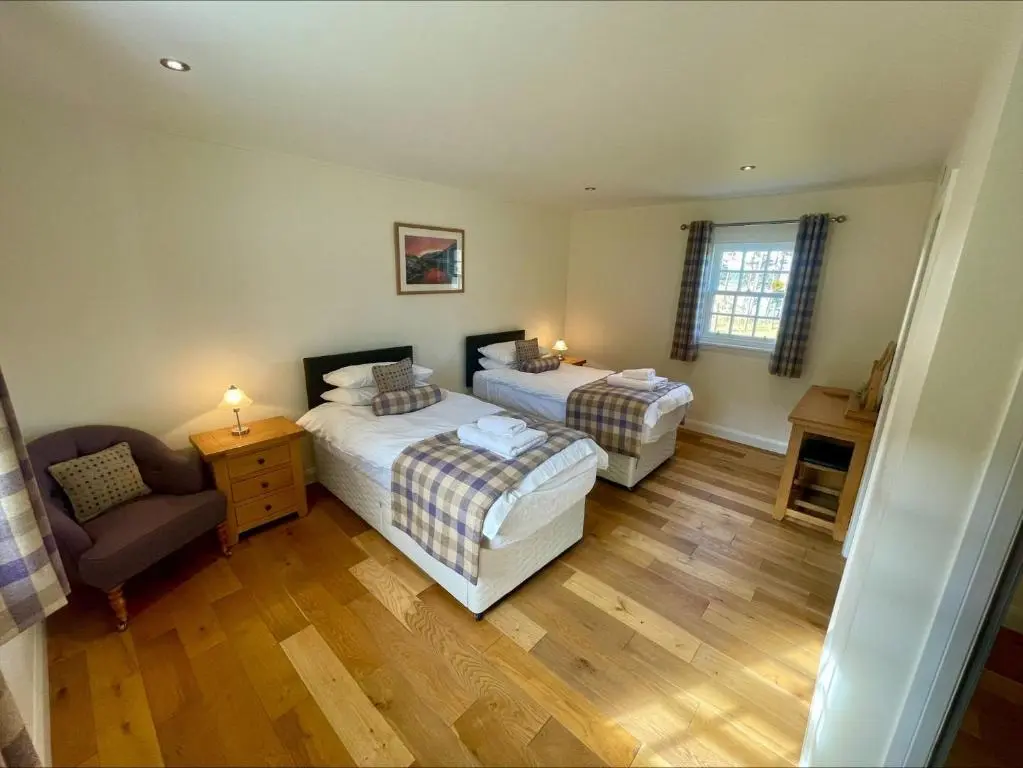 a room with two beds and a chair in it at Sherrabeg Cottage in Laggan