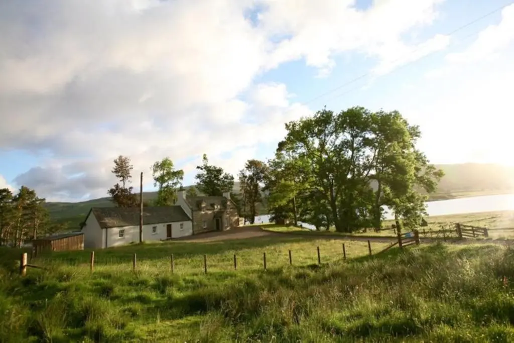 a house on a grassy hill with a fence at Sherrabeg Cottage in Laggan