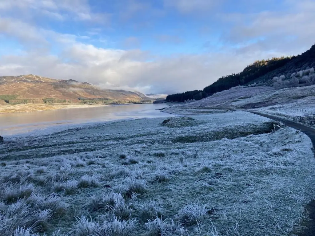 a river with snow on the ground and grass at Sherrabeg Cottage in Laggan