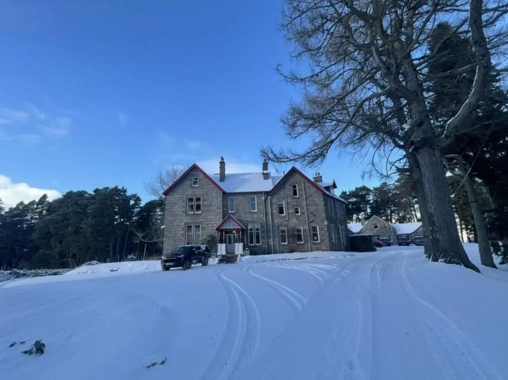 an old house in the snow with a car parked in front at Sherramore Lodge in Laggan