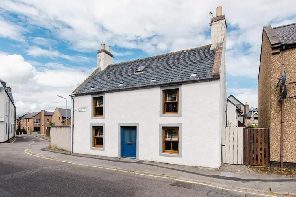 a white house with a blue door on a street at Weavers Cottage in Inverness