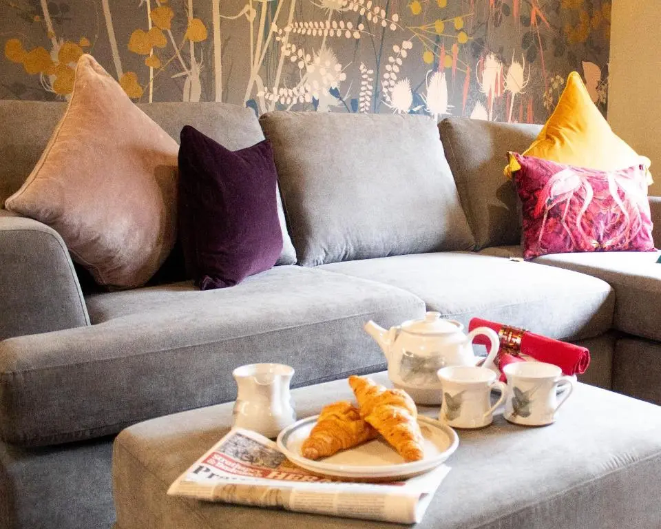 a couch with a table with a plate of croissants on it at Telford Cottage in Kincraig