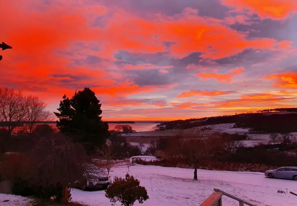 a sunset over a snowy field with a car at Strathview Lodge B&B in Dornoch