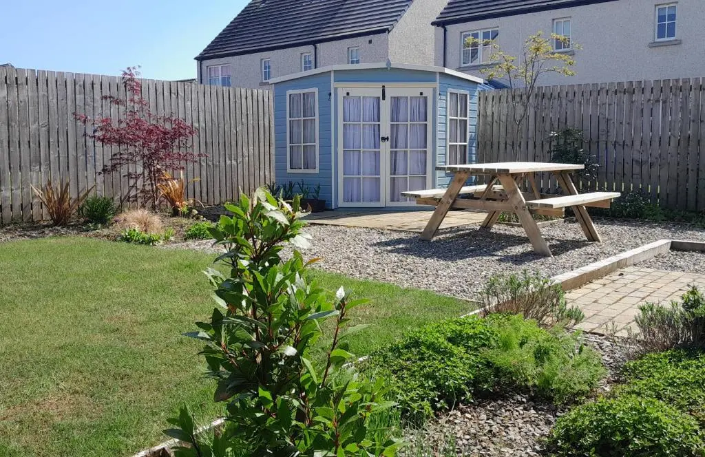 a wooden picnic table in a garden with a fence at No1Dornoch in Dornoch