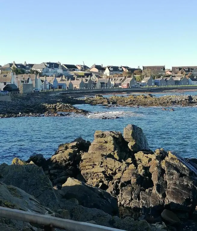 a body of water with rocks and houses in the background at Hytheview Cottage Whitehills in Whitehills