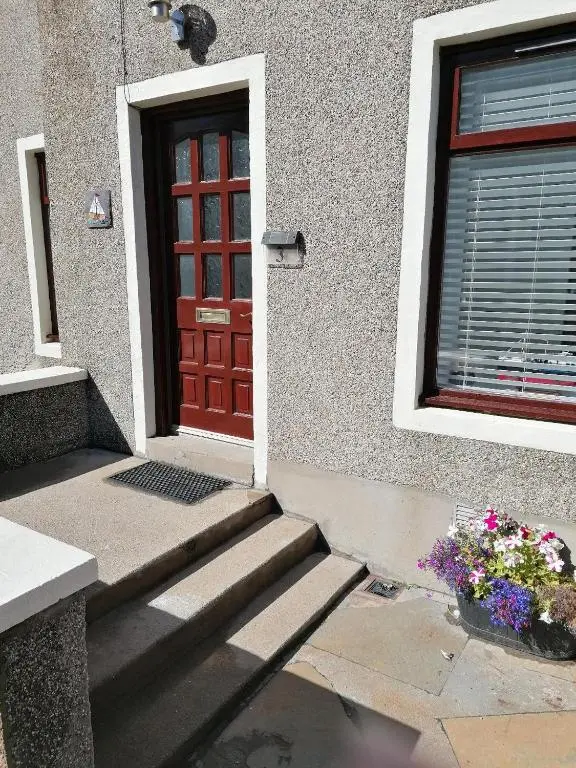 a red door of a house with a window and flowers at Hytheview Cottage Whitehills in Whitehills