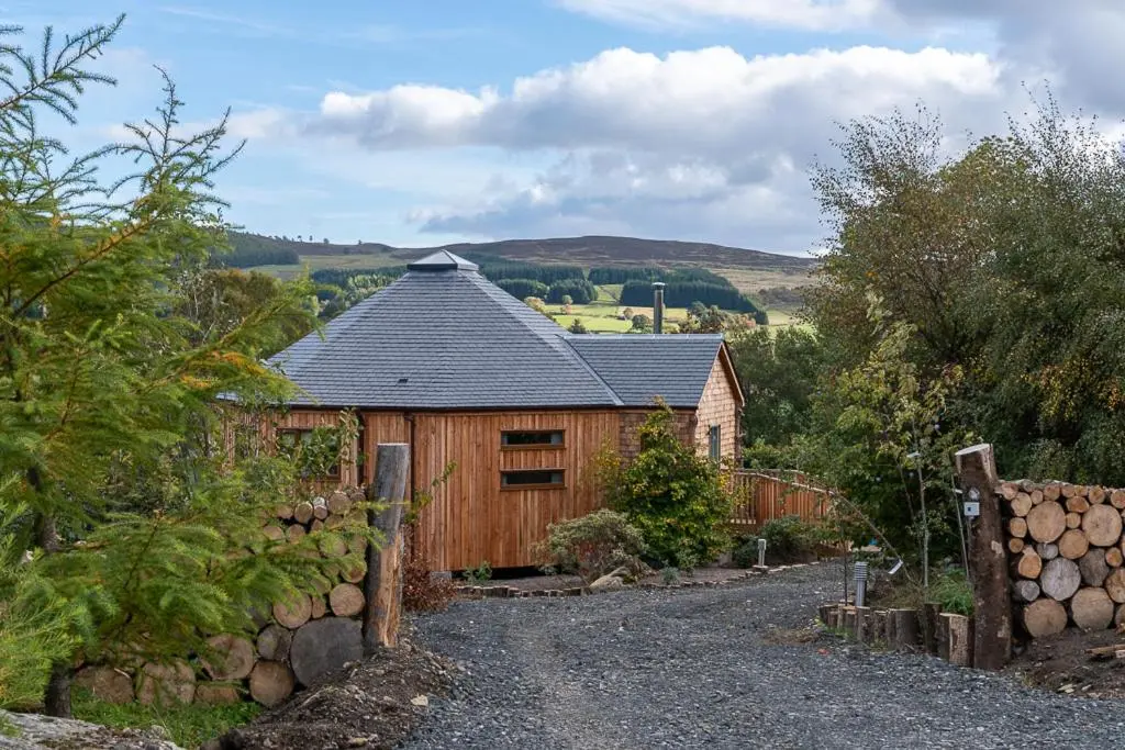 a wooden barn with a fence next to a road at Dalnoid Cottages & Treehouses Nr Glenshee in Glenshee