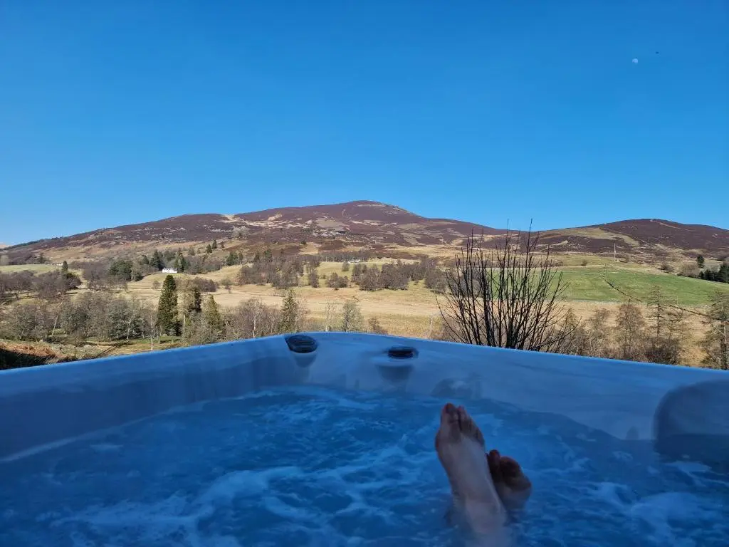 a person in a hot tub with their feet in it at Dalnoid Cottages & Treehouses Nr Glenshee in Glenshee