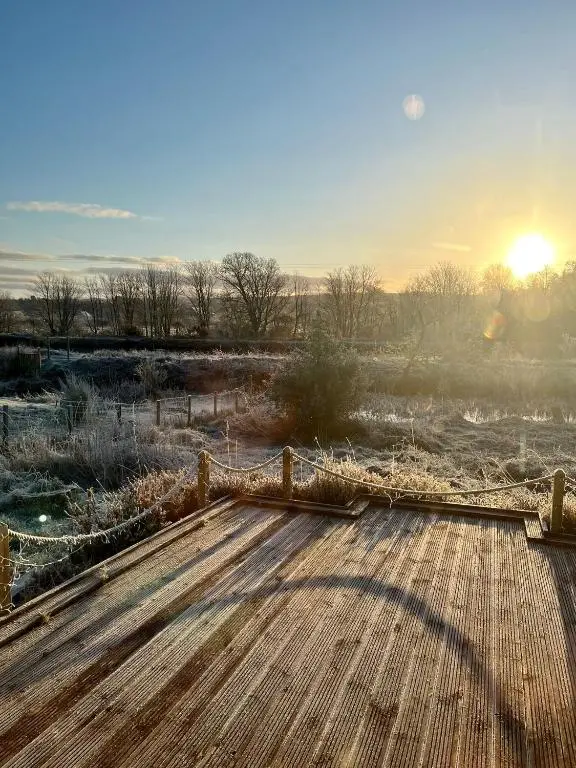 a wooden boardwalk in a field with the sun setting at Canal Side Cottage,on the banks of the Caledonian Canal in Inverness
