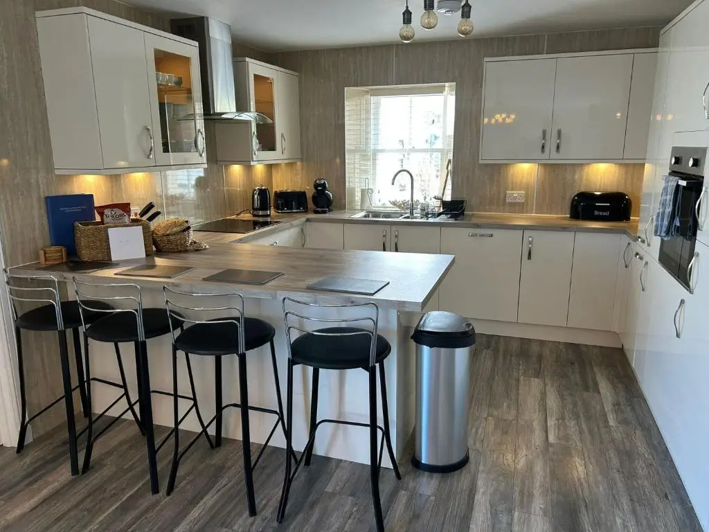 a kitchen with white cabinets and a counter with bar stools at Findochty Beach house - Private Garden-BeachFront in Buckie