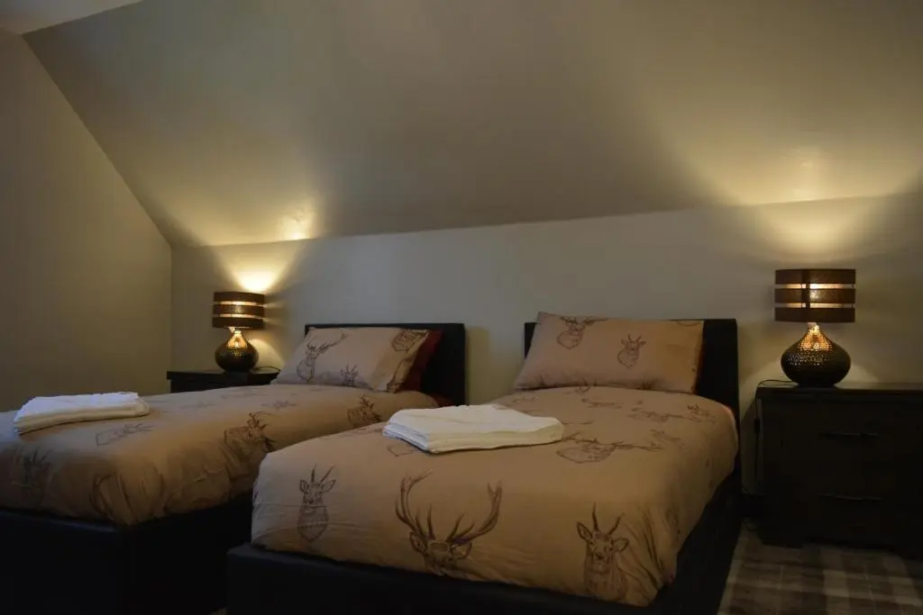 two beds in a room with two lamps on the wall at Appin House B&B in Fort Augustus