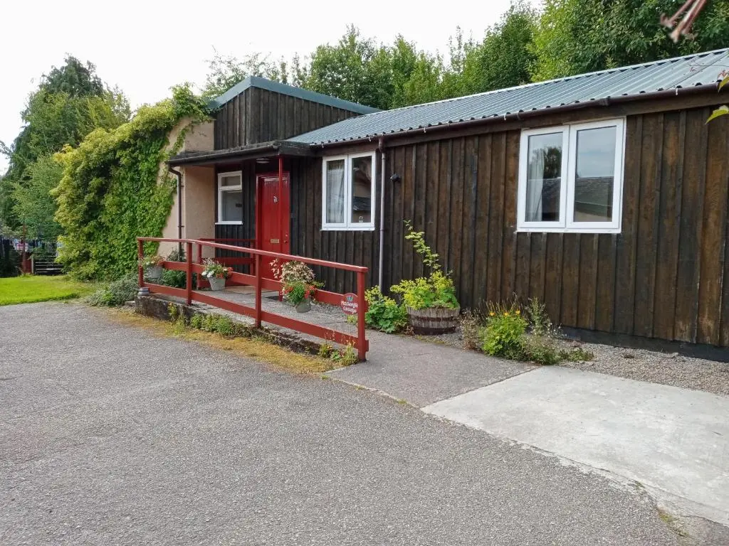 a small house with a red door and a driveway at Strathpeffer Holiday Cottages in Strathpeffer