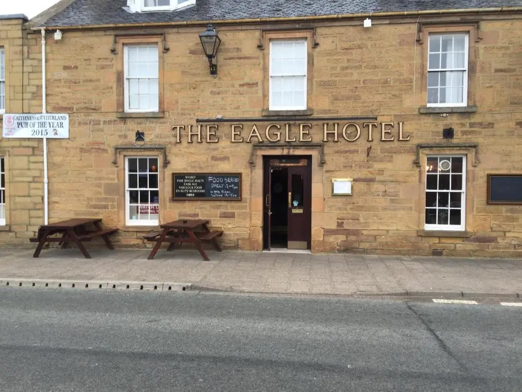 a building with benches in front of the eagle hotel at Eagle Hotel in Dornoch