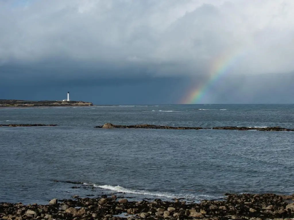 a rainbow over the water with rocks in the ocean at Apartment Harbour Nights Deluxe 7F by Interhome in Lossiemouth