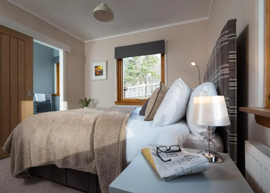 a bedroom with a bed with a table with a lamp at Cairn Eilrig - Seasgair Lodges in Loch Morlich