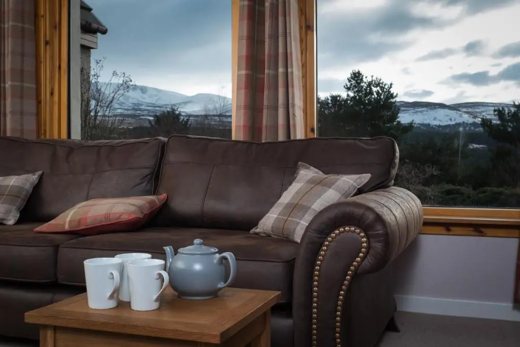 a brown couch sitting in front of a window at Cairn Eilrig - Seasgair Lodges in Loch Morlich